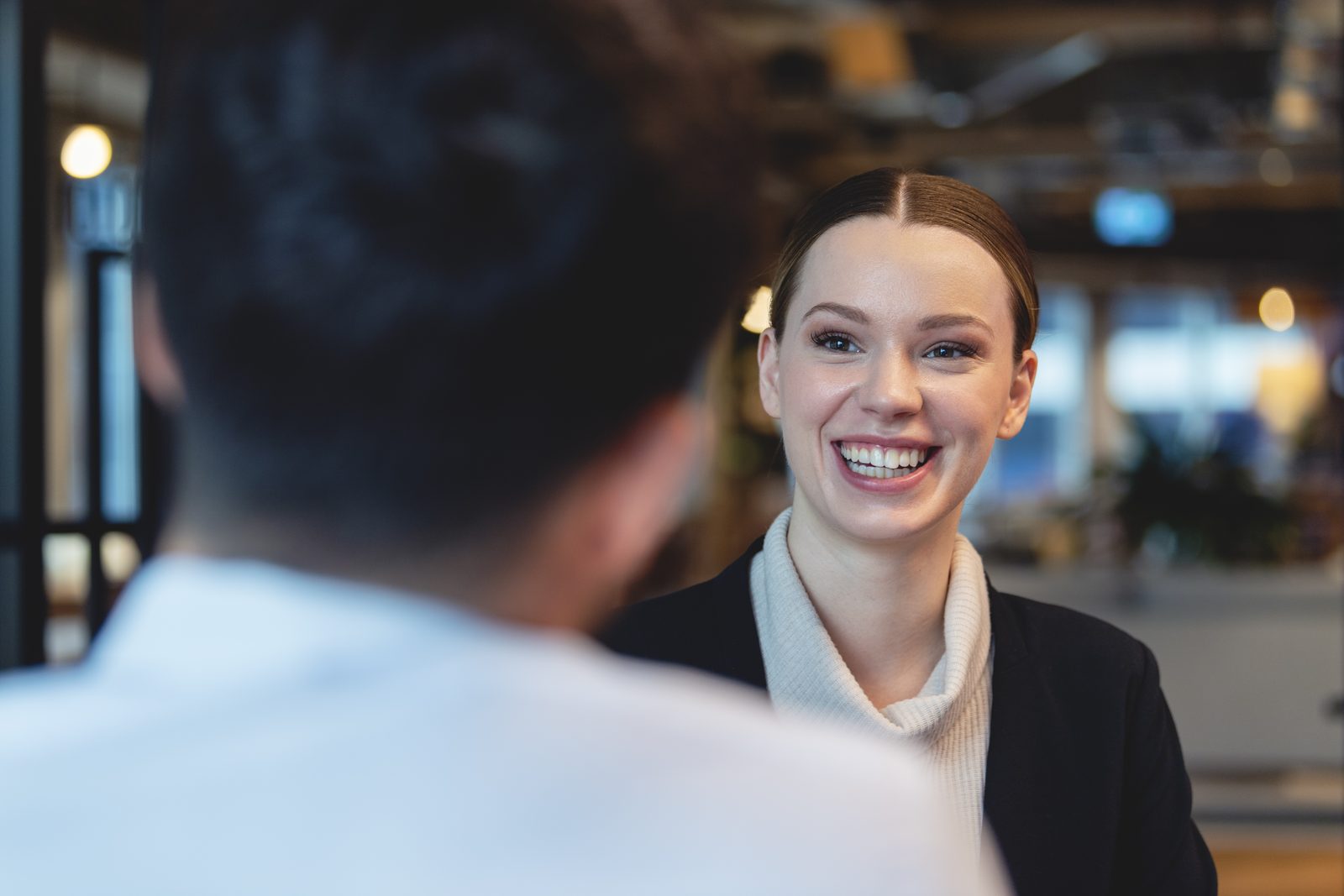 Smiling woman facing a man in a professional setting, engaging in a friendly conversation in an office.