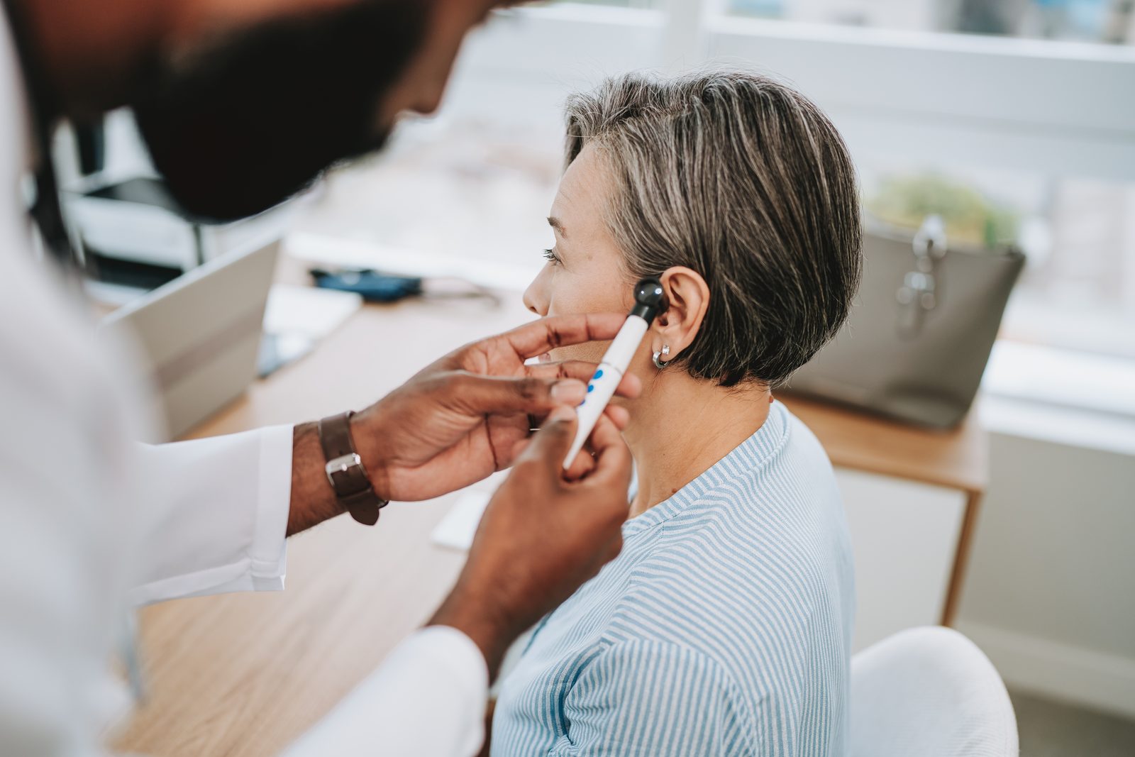 Healthcare professional adjusting a hearing aid on an older woman's ear in a bright clinic.