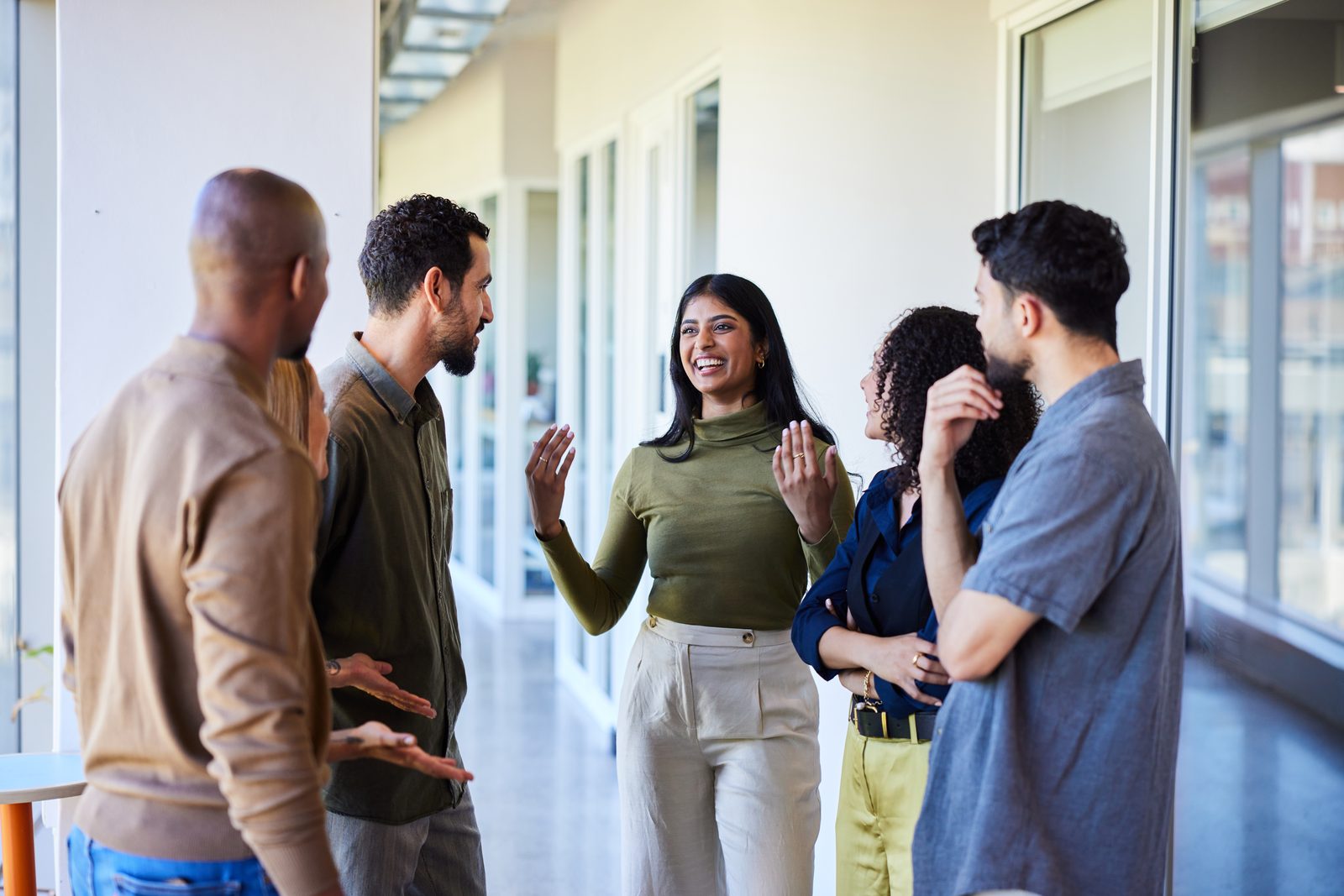 Group of five coworkers chatting and smiling in a bright hallway.