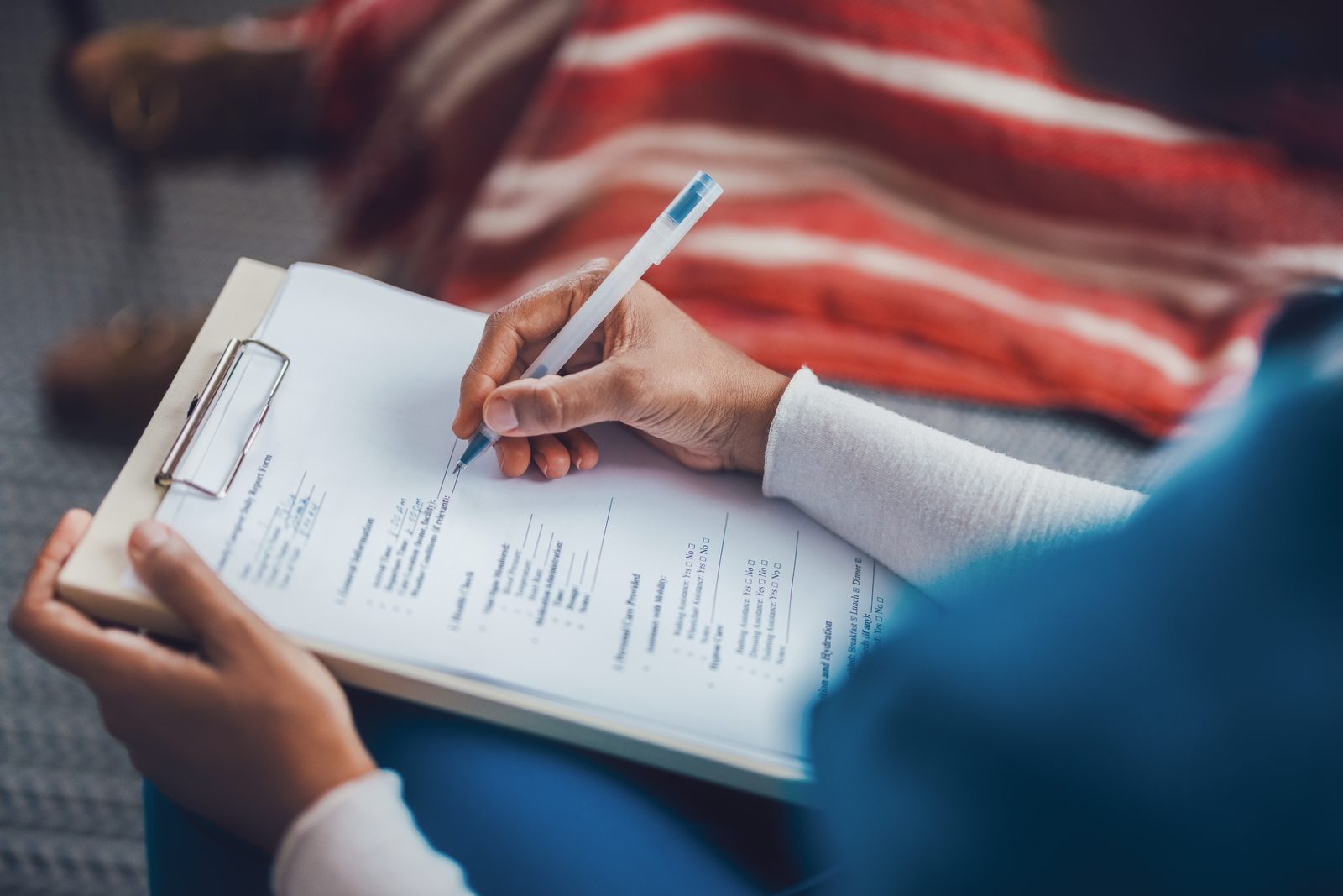 Person writes on a form held on a clipboard with a pen in hand, focus on filling out documents.