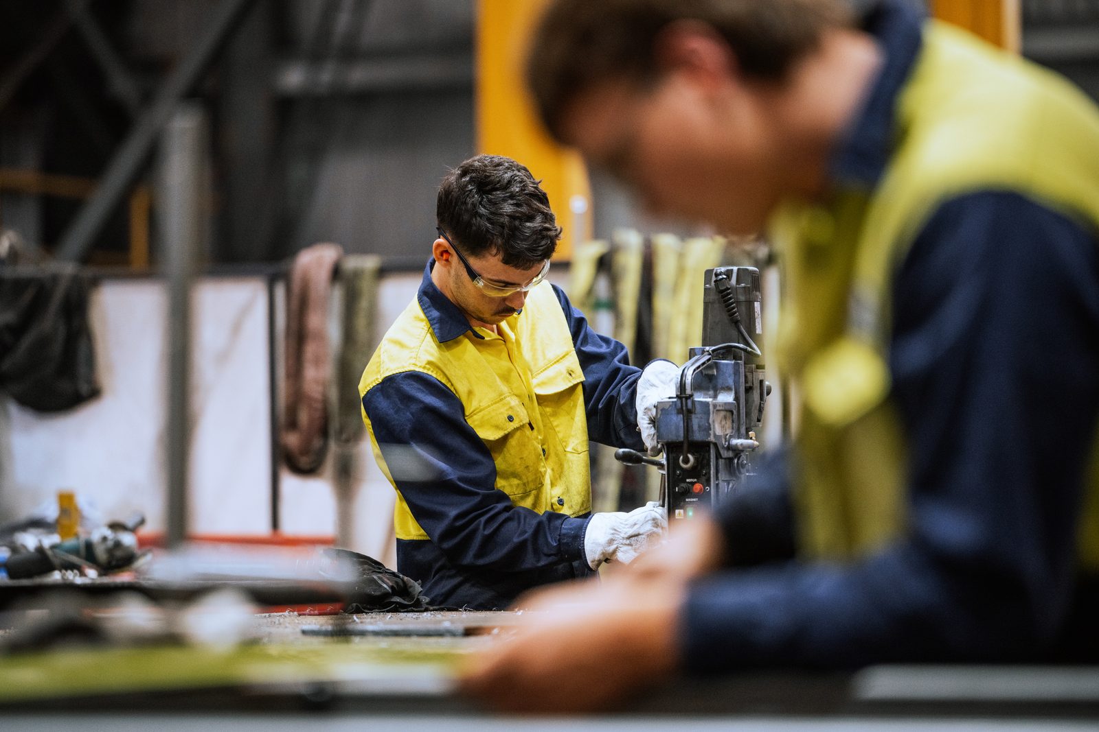 Worker in yellow safety vest and gloves operates a machine tool in a workshop, focused on the task.