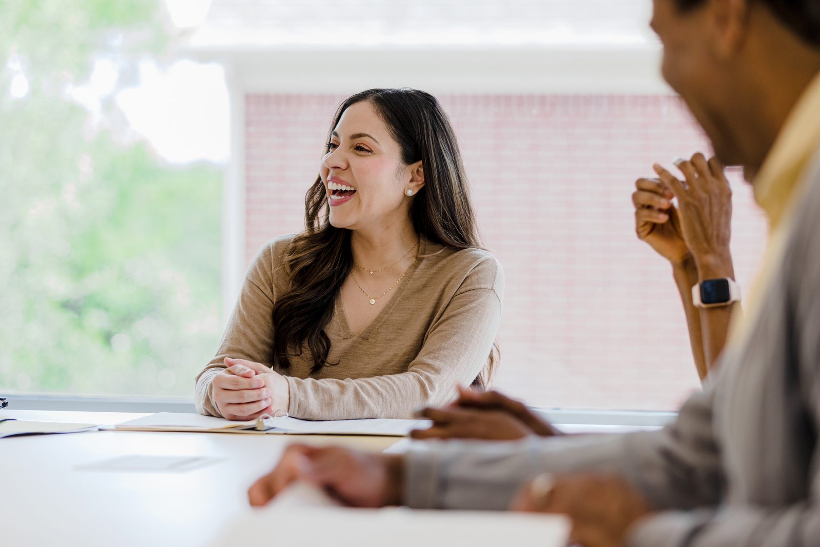 Woman laughing and talking at a conference table with colleagues in a bright meeting room.
