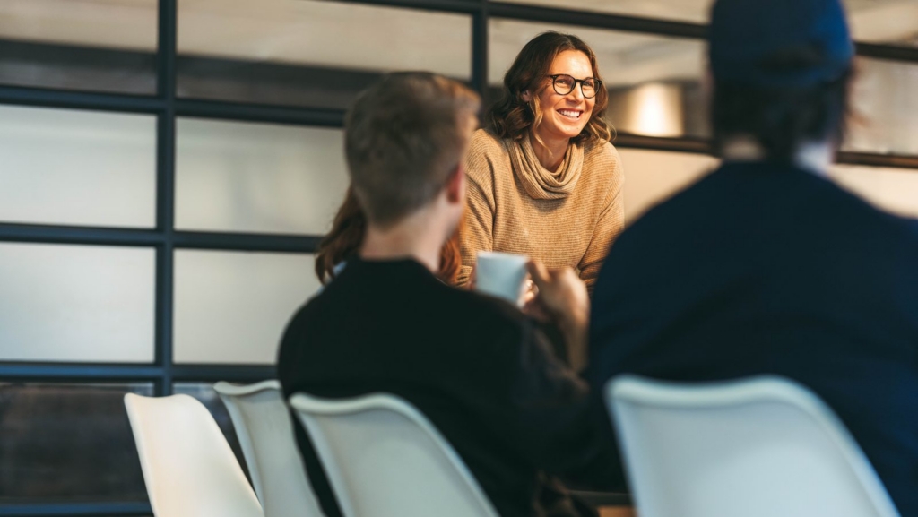Smiling woman wearing glasses talks with a small group in a modern office setting.
