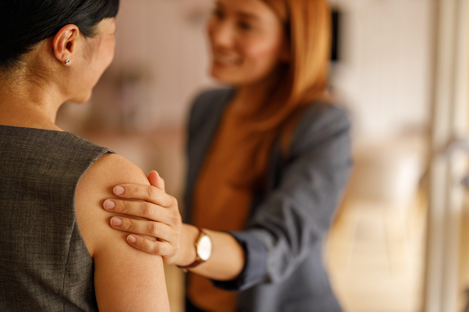 Clinician resting a hand on a woman's shoulder in a blurred hallway, conveying care or examination.