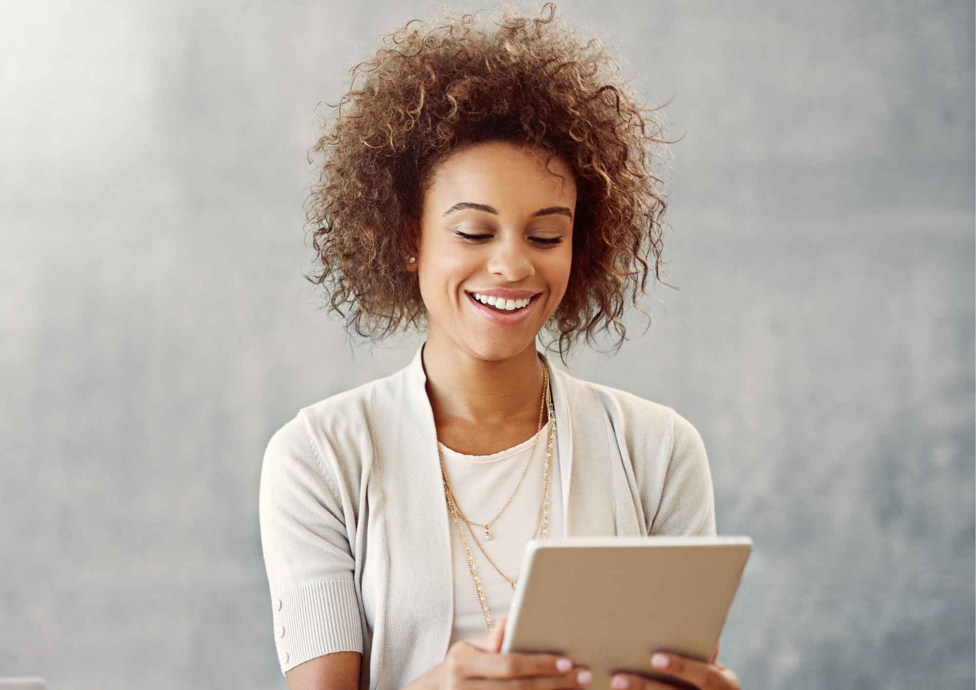 Smiling woman with curly hair holding a tablet and looking downward