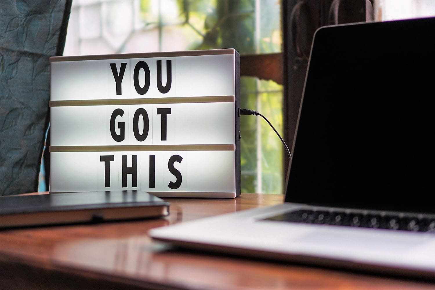 Motivational sign reading 'YOU GOT THIS' on a desk beside a laptop and notebook