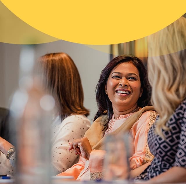 Smiling woman in peach blouse talking with colleagues at a meeting table